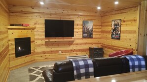 Ein gemütliches Blockhaus-Interieur mit Kamin, Flachbildfernseher und zwei Ledersofas.