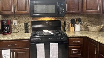 Una cocina con armarios de madera oscura, un microondas negro, una estufa con dos toallas y una cafetera.
