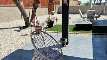 Una silla colgante con cojín, una mesita con un cuenco y una lámpara colgante.