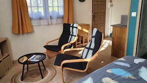 Een kamer met twee zwarte fauteuils, een kleine ronde tafel, een bed met een blauw-witte deken en een houten kast.