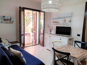 Ein Wohnzimmer mit Sofa, Esstisch, Stühlen, Fernseher und einem Balkon mit Blick.