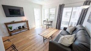 A living room with a sofa, a coffee table, a TV mounted on the wall, a dining table with chairs, and a window with curtains. - Updated Oceanview Modern Decor, Private Balcony! (North Myrtle Beach)