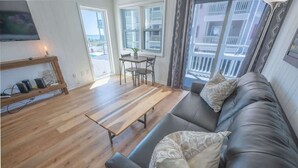 A living room with a sofa, a wooden coffee table, a TV on a stand, and a window with blinds. - Updated Oceanview Modern Decor, Private Balcony! (North Myrtle Beach)