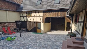 A courtyard with a paved floor, a wooden bench, a red lounge chair, and a green kiddie pool.