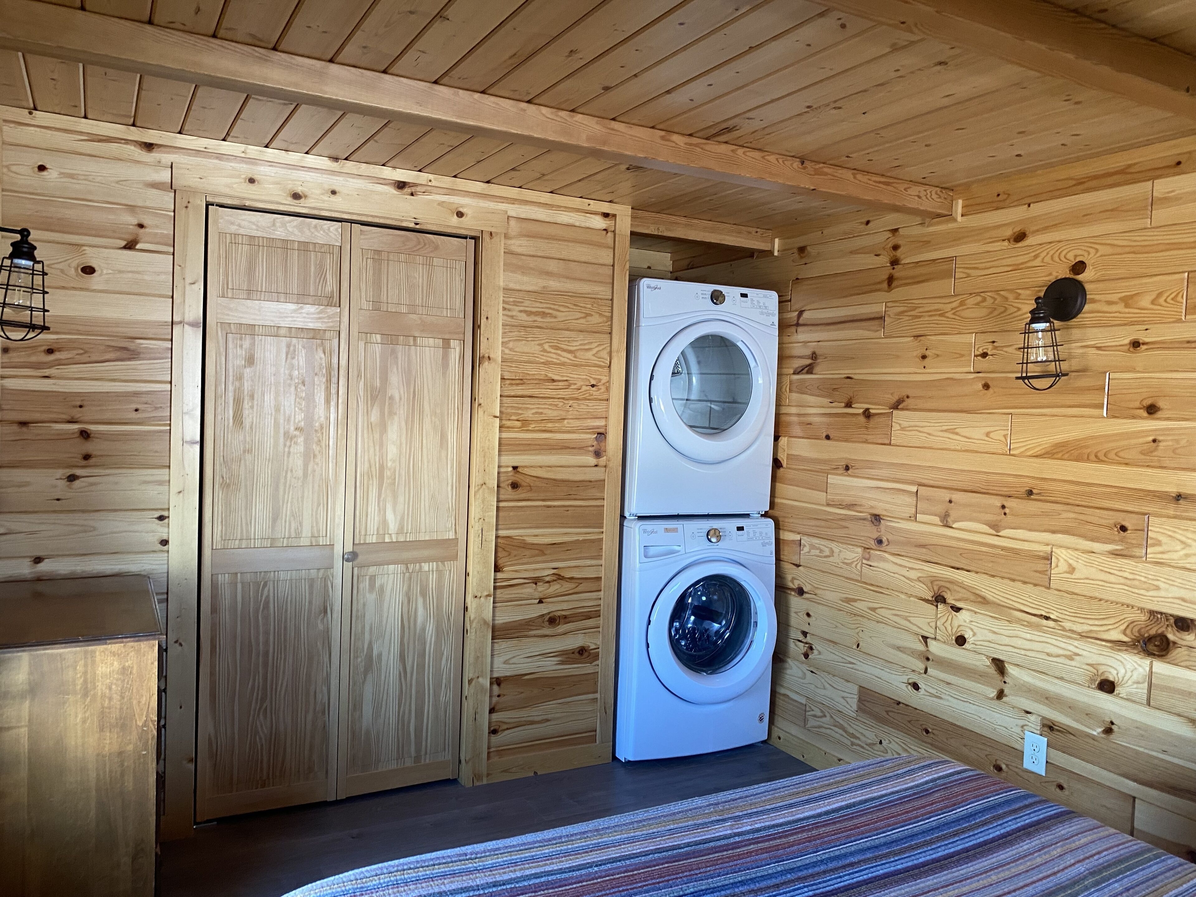 Een kleine kamer met houten wanden, een dubbele deur en een gestapelde wasmachine en droger.