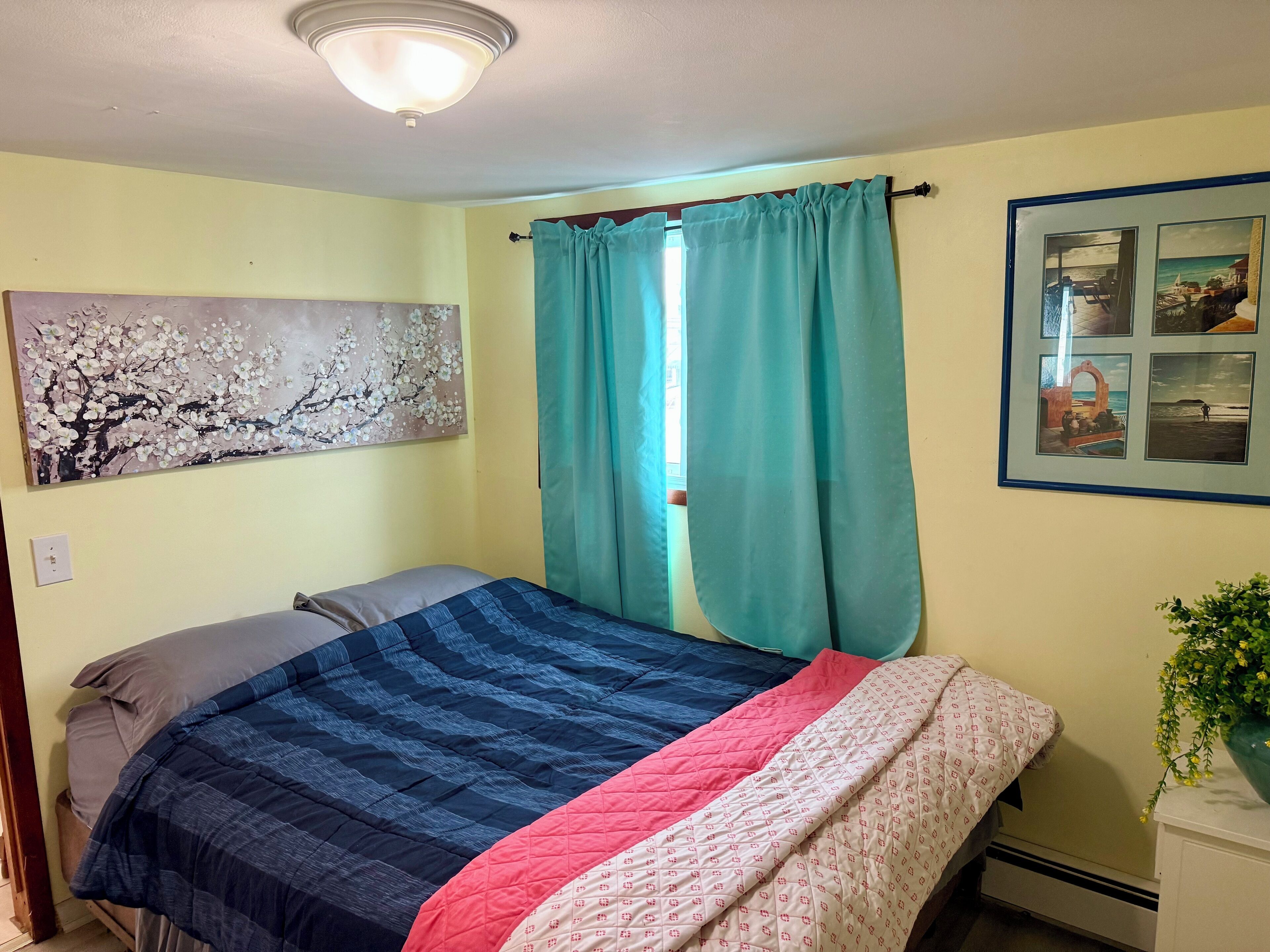A bedroom with a bed, teal curtains, a wall painting, and a framed photo.