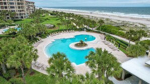 A resort with a central swimming pool, a beach, and a large building in the background. - AMELIA ISLAND RESORT - TURTLE DUNES OCEANFRONT CONDO WITH POOL/TENNIS (Fernandina Beach)
