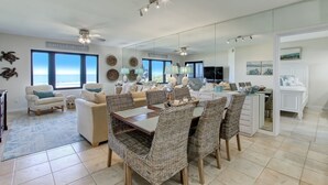 A spacious living room with a large dining table, comfortable seating, and a view of the ocean. - AMELIA ISLAND RESORT - TURTLE DUNES OCEANFRONT CONDO WITH POOL/TENNIS (Fernandina Beach)