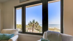 A room with two white armchairs, a small round table, and a view of the beach through large windows. - AMELIA ISLAND RESORT - TURTLE DUNES OCEANFRONT CONDO WITH POOL/TENNIS (Fernandina Beach)