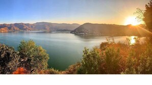 Een panoramisch uitzicht op een meer, met bergen op de achtergrond en een zonsopgang of zonsondergang aan de horizon.