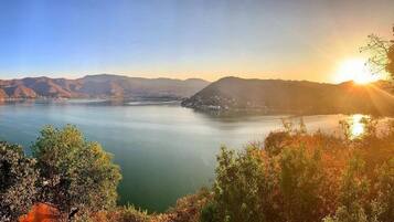 A panoramic view of a lake with mountains in the background and a sunrise or sunset on the horizon.