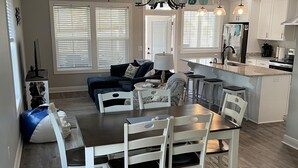Een moderne keuken met witte kasten, een centraal eiland en een eetgedeelte met een tafel en stoelen.