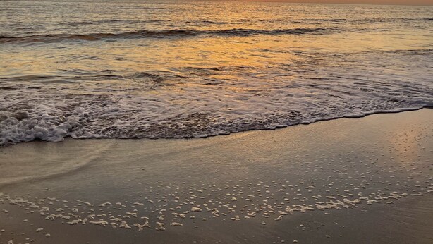 Een strand met golven en een zonsondergang.