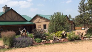 A lodge with a green roof, a stone chimney, and a landscaped garden with deer statues. - Forest Estate Guest Quarters-Seclusion- Just Minutes from Town (Woodland Park)