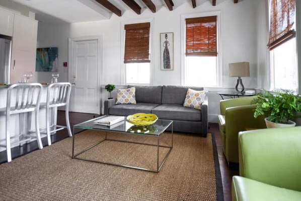 Ein modernes Wohnzimmer mit Glastisch, grauem Sofa und grünem Sessel.