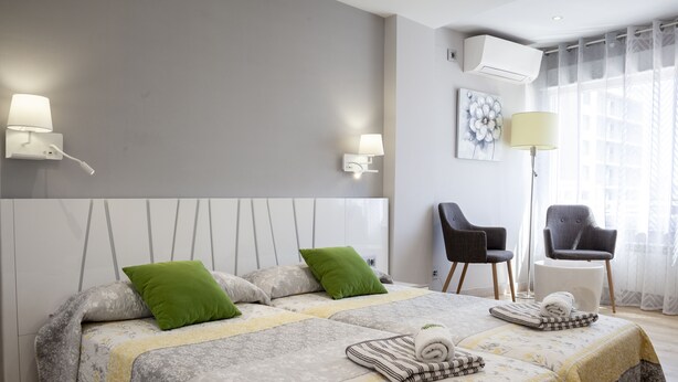 A modern hotel room with two beds, a sitting area with chairs, and a large window with curtains.
