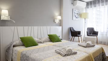 Ett modernt hotellrum med två sängar, en sittgrupp med stolar och ett stort fönster med gardiner.