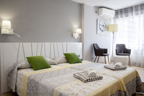 A modern hotel room with two beds, a sitting area with chairs, and a large window with curtains.