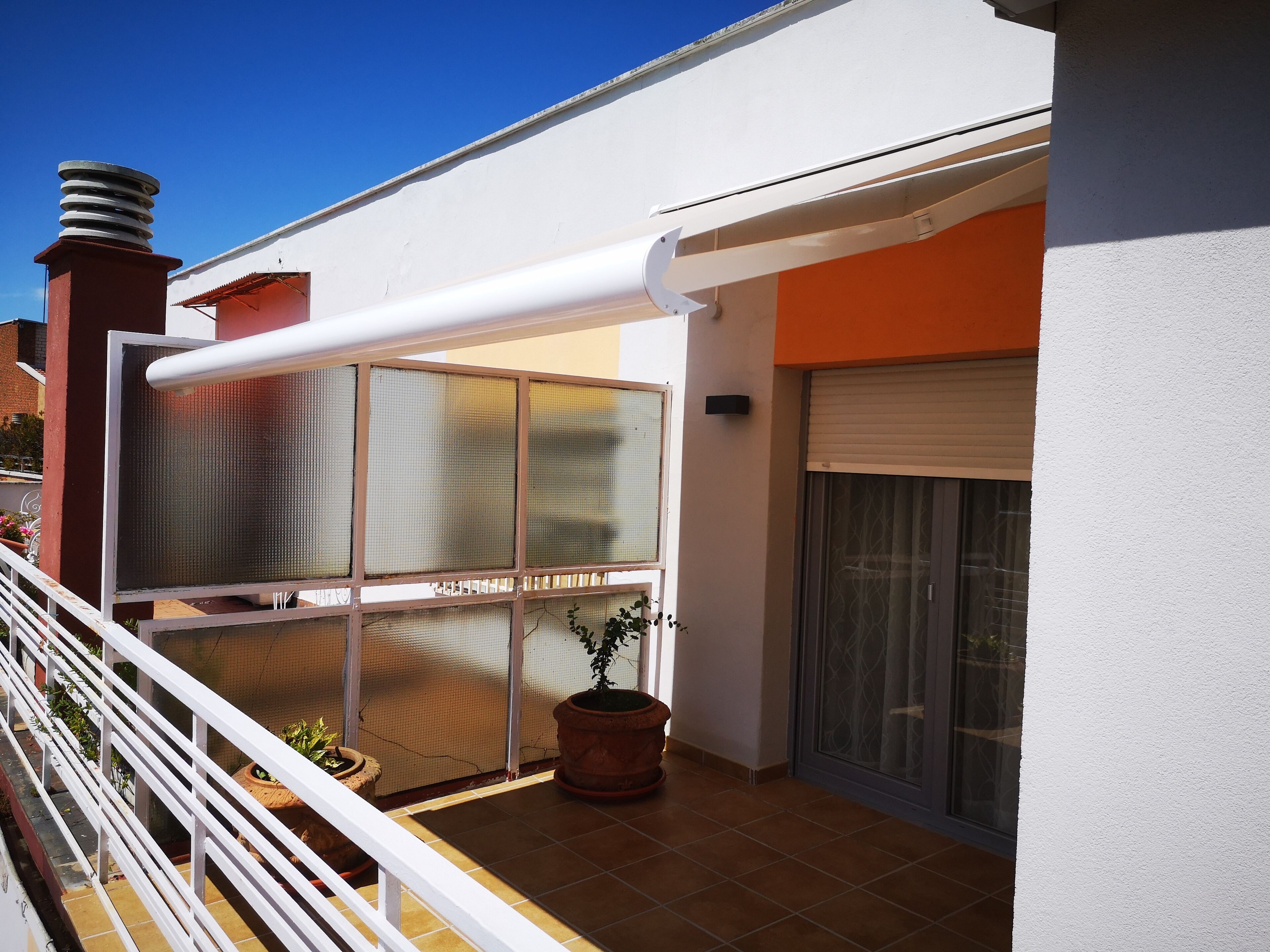 Un balcon avec une balustrade blanche, une grande fenêtre et un pot de fleurs.
