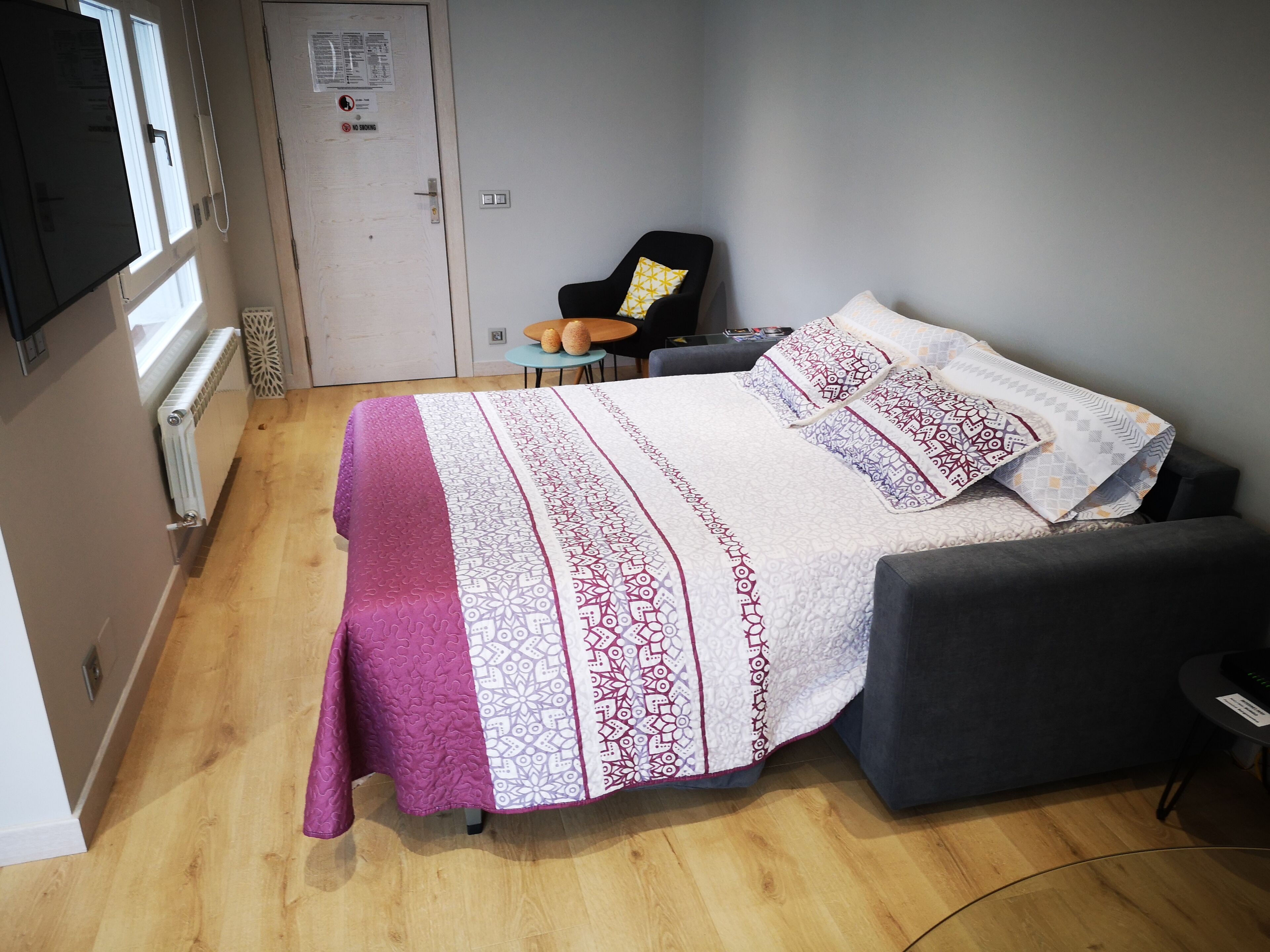 Une chambre à coucher avec un lit, une chaise, une petite table et une porte sur laquelle est apposée une pancarte.