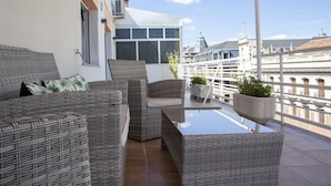 A balcony with wicker furniture, potted plants, and a view of city buildings.