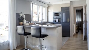 A modern kitchen with a central island, two bar stools, a refrigerator, an oven, and a microwave.