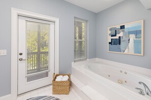 Une salle de bain avec une baignoire blanche, un panier en osier rempli de serviettes et un tableau accroché au mur.
