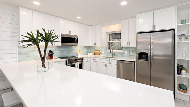 Una cocina moderna con armarios blancos, electrodomésticos de acero inoxidable y una isla central con una planta.