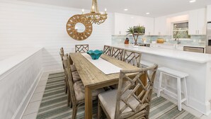 Una cocina moderna con armarios blancos, una isla central y un comedor con mesa y sillas de madera.
