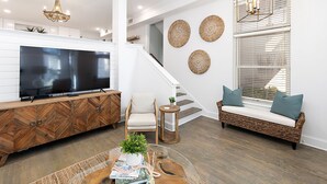 Una sala de estar moderna con un televisor de pantalla plana grande, un mueble de madera con diseño en espiga, un sofá de mimbre con cojines y una escalera con arte decorativo en la pared.