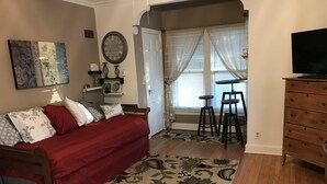 Un dormitorio con cama, televisor, cómoda y ventana con cortinas traslúcidas.
