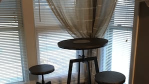 Rincón con una mesa redonda y dos taburetes, un tapete estampado y una ventana con persianas.