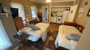 Un dormitorio pequeño con dos camas, un escritorio, una silla y una kitchenette.