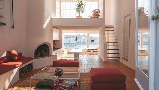A spacious living area with a fireplace, red furniture, a glass coffee table, and a view of the sea.