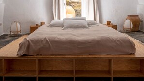 A bedroom with a wooden bed, a stone wall, and a window with curtains.