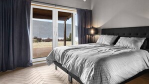 A bedroom with a bed, a nightstand, a lamp, and a view of a natural landscape through a sliding door. - Cottage - Sleeps 14 With Fjord Views (Frogn)