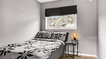 A bedroom with a bed, a nightstand with a lamp, a window with a view of a rocky landscape, and a black curtain.
