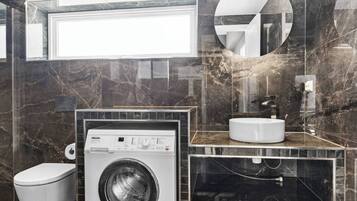 A modern bathroom with a washing machine, a toilet, a sink, and a mirror.