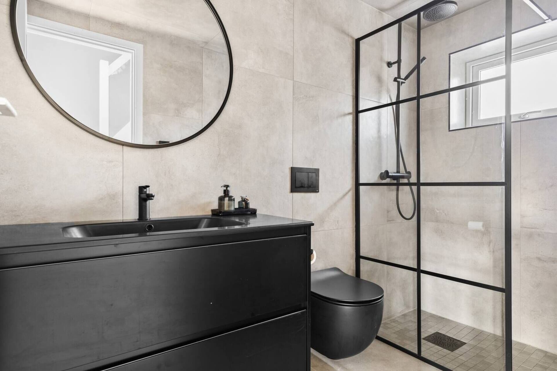 Un bany modern amb un lavabo negre, un mirall rodó, una cabina de dutxa de vidre i un vàter.