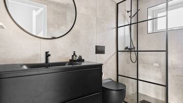 Un bany modern amb un lavabo negre, un mirall rodó, una cabina de dutxa de vidre i un vàter.
