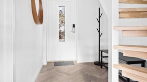 A modern interior with a white door, a herringbone wood floor, a black coat rack, and a wooden staircase. - Cottage - Sleeps 14 With Fjord Views (Frogn)