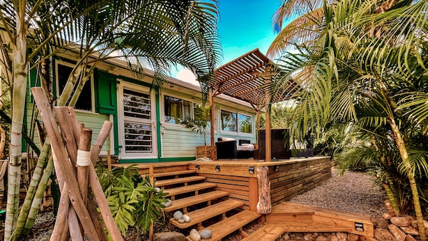 A wooden deck with a stone pathway leading to a covered seating area with a view of a green house. - Jungle Cottage Orient Bay: Charming and authentic (Saint Martin)
