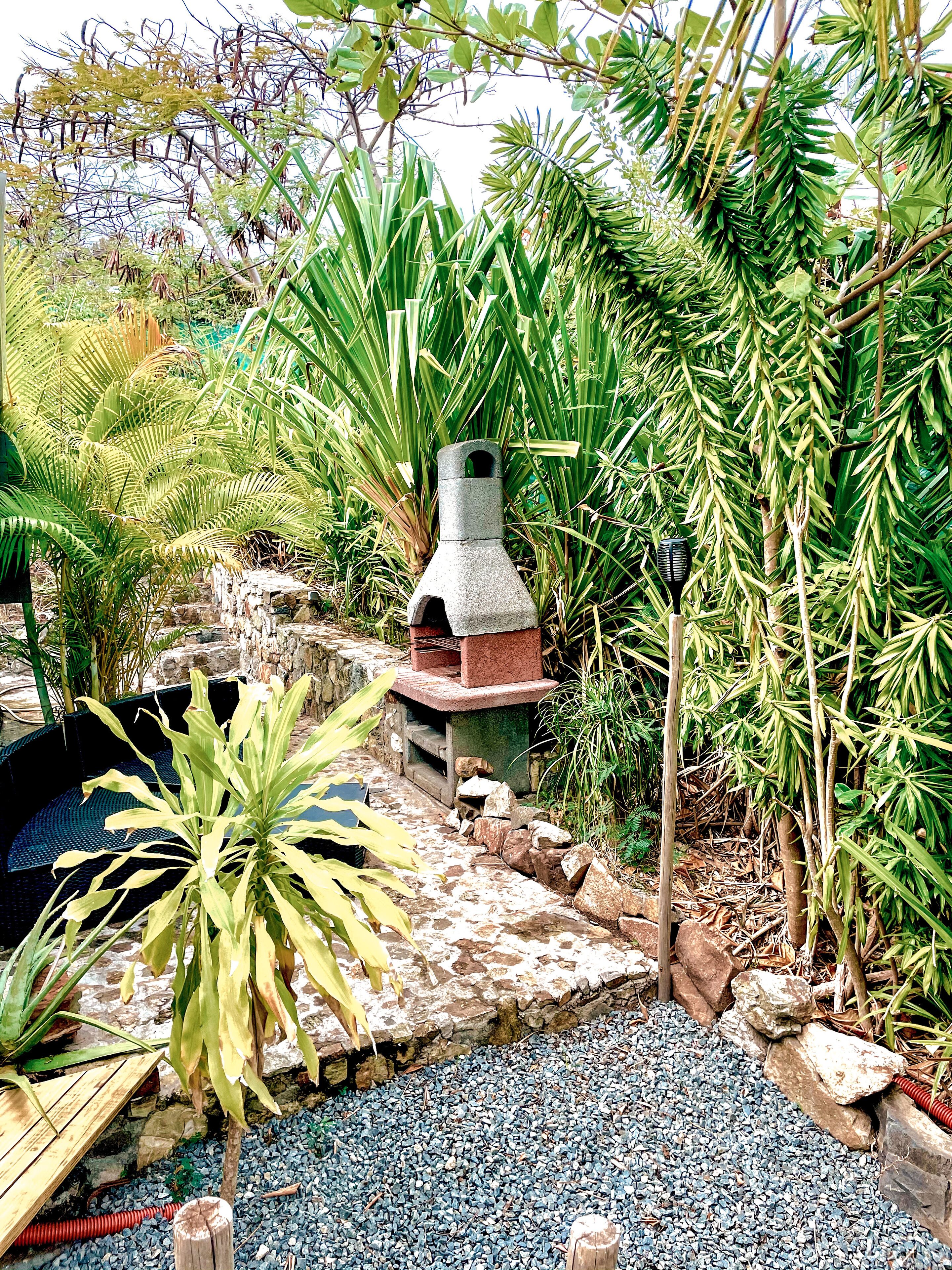 A garden with a stone barbecue grill, a wooden bench, and various plants.