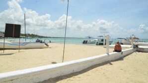 A beach with boats docked, a white wall, and a person sitting on the wall. - Residencial Lakis 1 (Boca Chica)