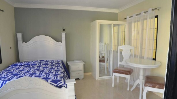 A bedroom with a bed, a bedside table, a chair, a table, and a wardrobe. - Residencial Lakis 1 (Boca Chica)