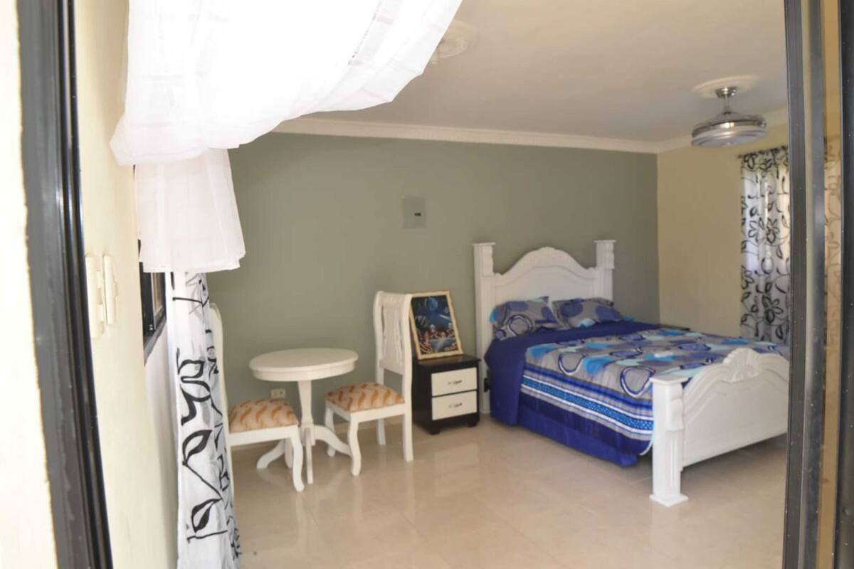 Une chambre à coucher avec un lit, une petite table, une chaise et une table de chevet.
