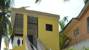 A two-story building with a yellow exterior, a staircase with metal railings, and a stone-tiled entrance. - Residencial Lakis 1 (Boca Chica)