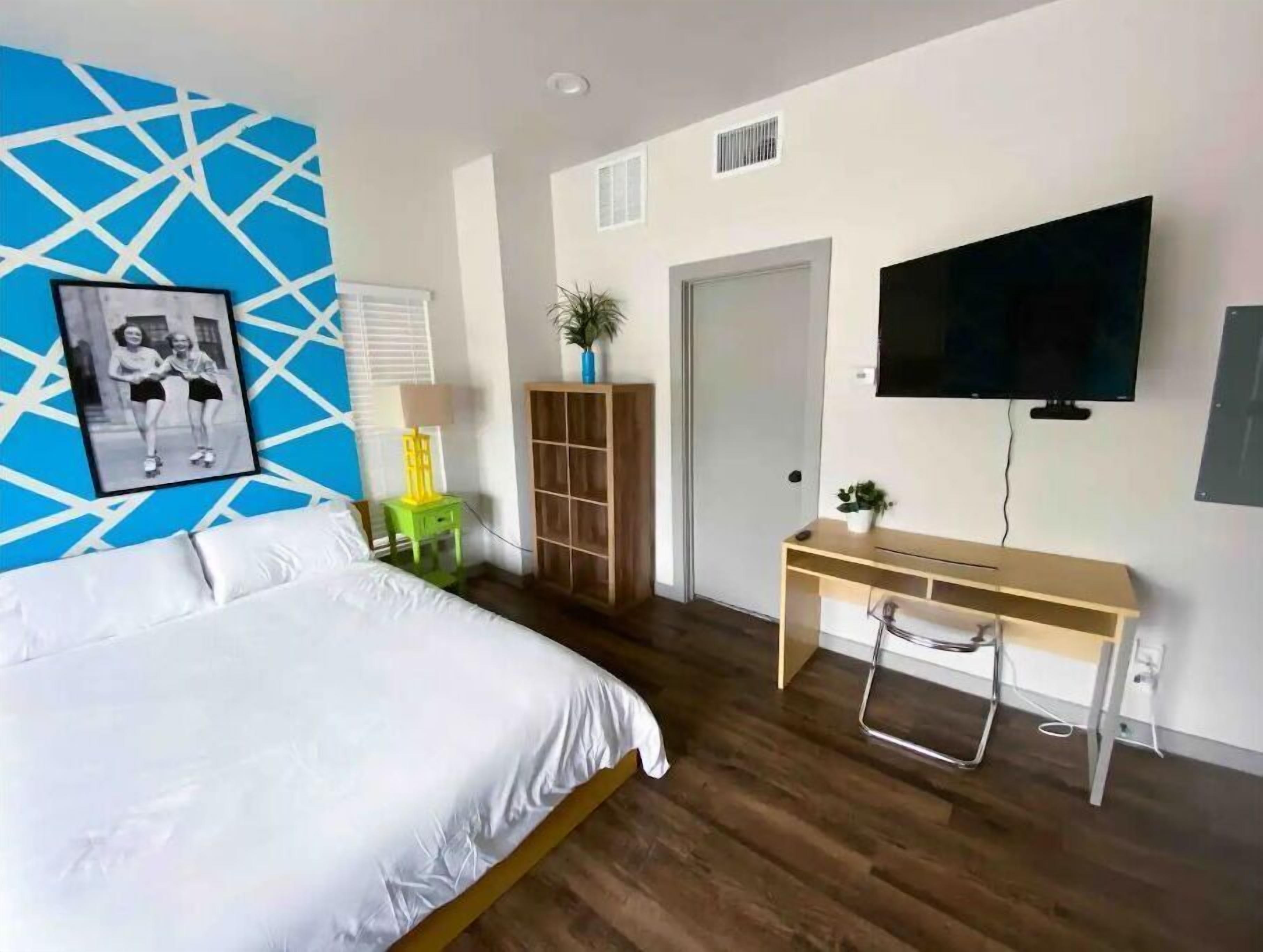 Een moderne slaapkamer met een bed, een bureau, een televisie en een blauw geometrisch wandontwerp.
