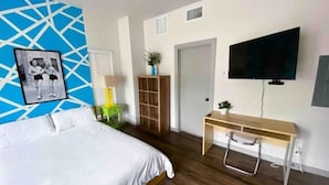 Una camera da letto moderna con un letto, una scrivania, una TV e un motivo geometrico blu sulla parete.