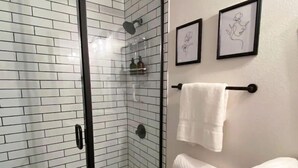 Un bagno con box doccia in vetro, pareti piastrellate di bianco, un WC e due quadri appesi alla parete.